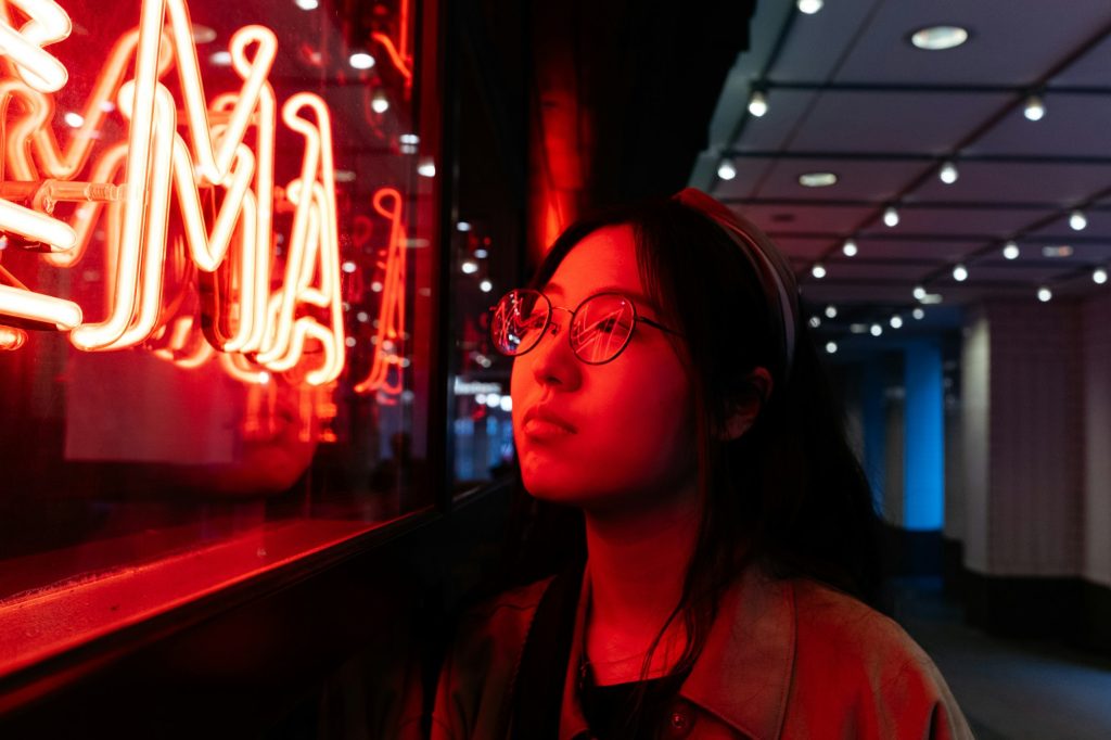 Young asian female wearing glasses in front of neon light sign, shallow selective focus