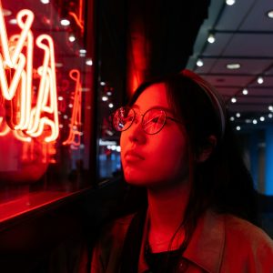 Young asian female wearing glasses in front of neon light sign, shallow selective focus